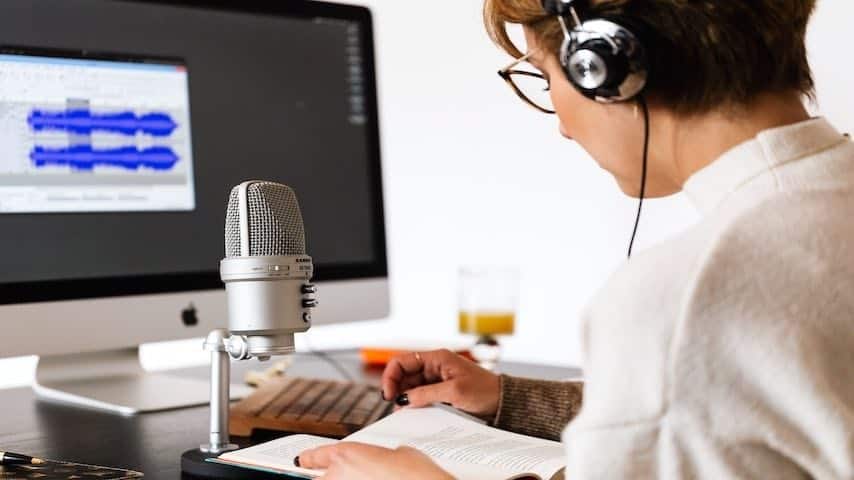 Guide to Vocal Warm-Ups for Voice Actors: Best Exercises and Tips. Photo of woman practising a script in front of a microphone and computer. Pexels License https://www.pexels.com/photo/person-reading-a-book-4476140/